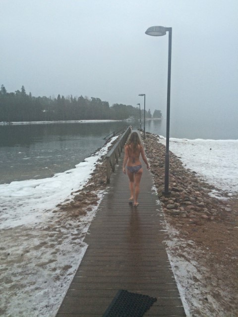 Frau mit langen Haaren läuft im Februar im Bikini zum Meer, umgeben von Schnee am Ufer, Nationalpark Ruissalo, Finnland