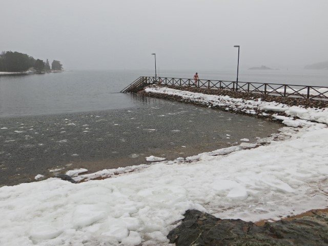 Frau läuft im Bikini über Steg am Meer, auf dem Wasser ist Eis, am Ufer Schnee, Nationalpark Ruissalo, Finnland