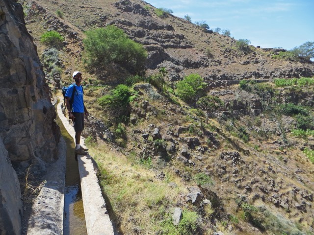 Farbiger Mann lacht auf einem schmalen Lavada-Weg über einem tief abstürzenden Tal auf Santo Antao, Kapverden