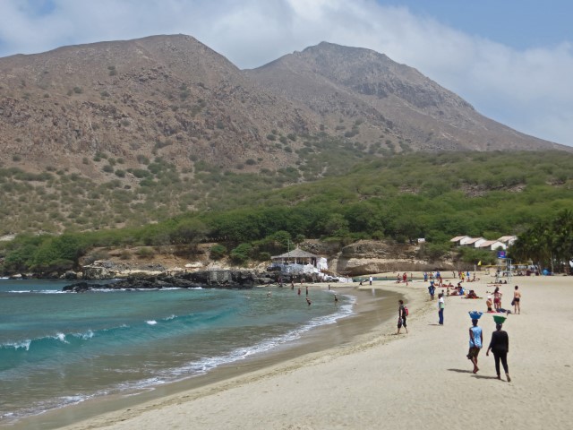 Weißer Sandstrand von Tarrafal, Kapverden, wo Verkäuferinnen Körbe auf den Köpfen tragen, im Hintergrund hohe trockene Berge