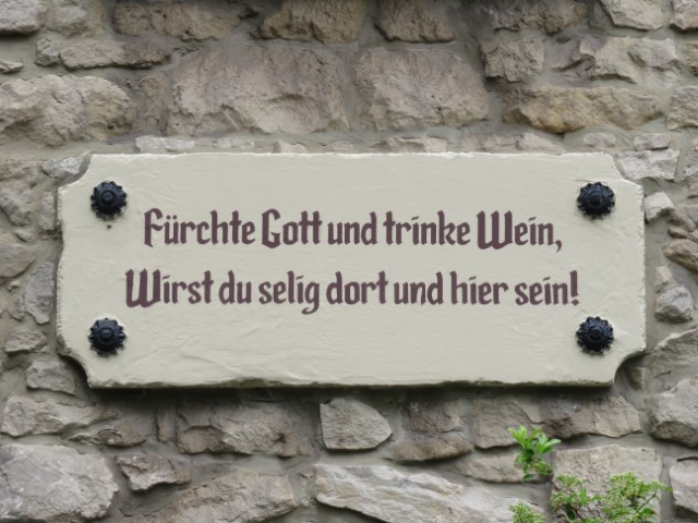 Helles Schild an einer Steinwand mit einem Spruch zu Wein und Glück in Luxemburg