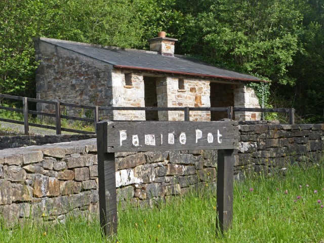 Schild mit "Famine Pot" in Irland und kleinem Steinhaus dahinter