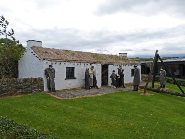 Kleines weißes Steinhaus mit Reetdach und Puppen davor im Doagh Famine Village in Irland