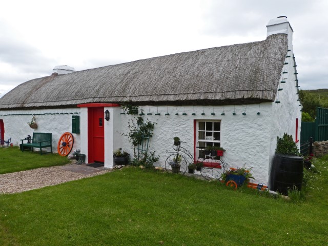 Flaches irisches Steinhaus in Weiß mit roter Tür und Reetdach, Donegal, Irland