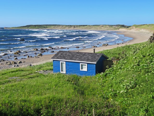 Blaue Holzhütte auf Wiese an einem langen Sandstrand im Gros Morne Nationalpark Neufundland