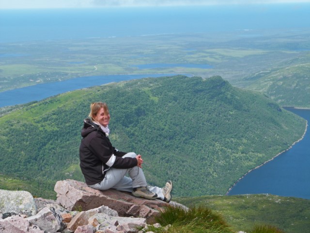 Strahlende junge Frau sitzt auf Felsspitze auf dem Gors Mourne Mountain, Gros Morne Nationalpark Neufundland