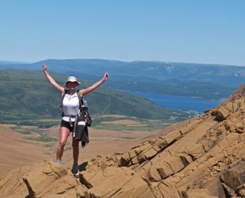 Junge Frau auf einem Berg im Grod Morne NP in Neufundland mit stolz erhobenen Armen