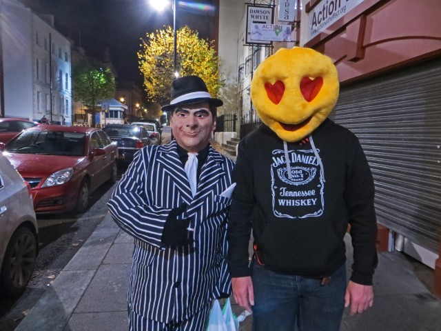 Zwei verkleidete Männer mit Maske und Anzug bzw. Smiley Face mit Herz-Augen an Halloween in Derry, Nordirland