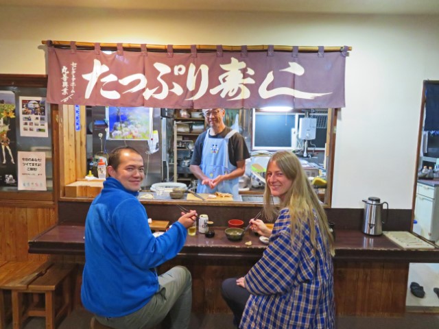 Homestay in Japan mit offener Küche, in der der Gastgeber Sushi macht, davor sitzen eine Deutsche und ein japanischer Guide