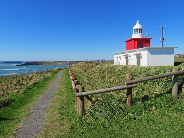 Weiß-roter Leuchtturm auf einer grünen Wiese am Cape Kiritappu, Hokkaido, Japan