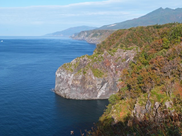 Blick über die felsige, bewachsene Küste im Shiretoko Nationalpark mit blauem Meer davor, Hokkaido, Japan