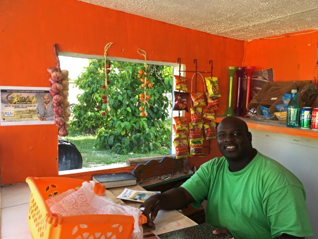 Mann in grünem Shirt verkauft in seinem orange gestrichenen Kiosk Snacks