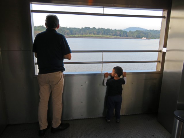 Mann und Kind schauen aus dem Panama Canal Railway auf den Panamakanal