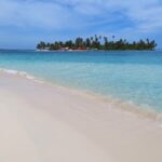 Blick über einen hellen Strand und türkisfarbenes Meer auf eine San Blas Insel in Panama