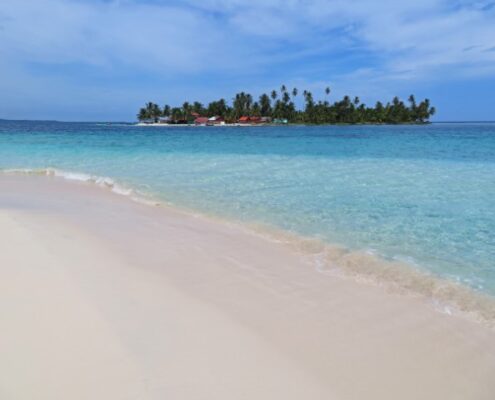 Blick über einen hellen Strand und türkisfarbenes Meer auf eine San Blas Insel in Panama