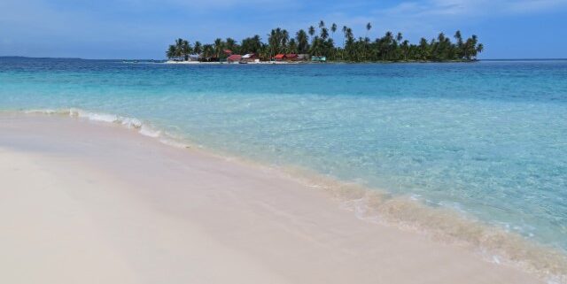 Blick über einen hellen Strand und türkisfarbenes Meer auf eine San Blas Insel in Panama