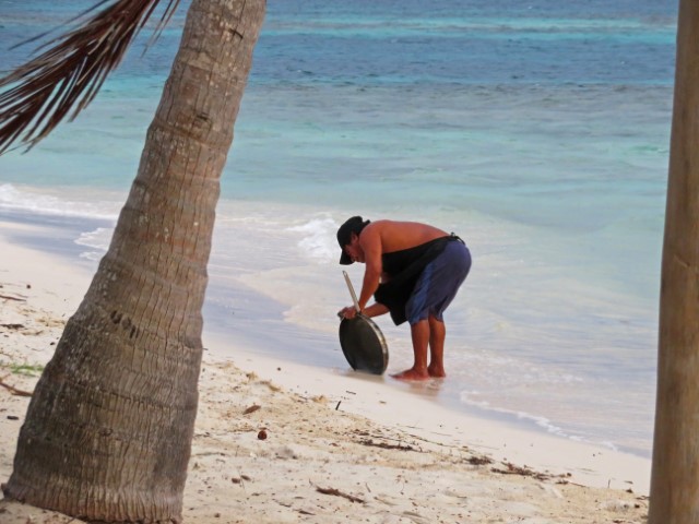 Mann mit nacktem Oberkörper wäscht eine große Pfanne im Meer