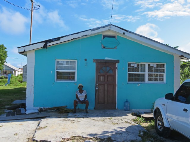 Türkisfarbenes Haus, vor dem eine Frau sitzt, auf Black Point Exuma