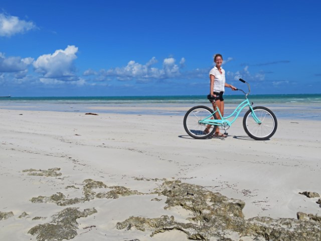 Junge Frau mit Fahrrad an einsamem weißen Sandstrand