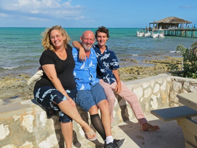 Vater mit seiner Tochter und dem Sohn sitzen auf einer Mauer vor dem türkisfarbenen Meer