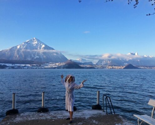 Junge Frau mit weißem Bademantelund Handtuch auf dem Kopf steht bei Schnee am Thuner See