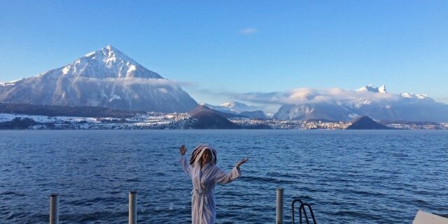 Junge Frau mit weißem Bademantelund Handtuch auf dem Kopf steht bei Schnee am Thuner See