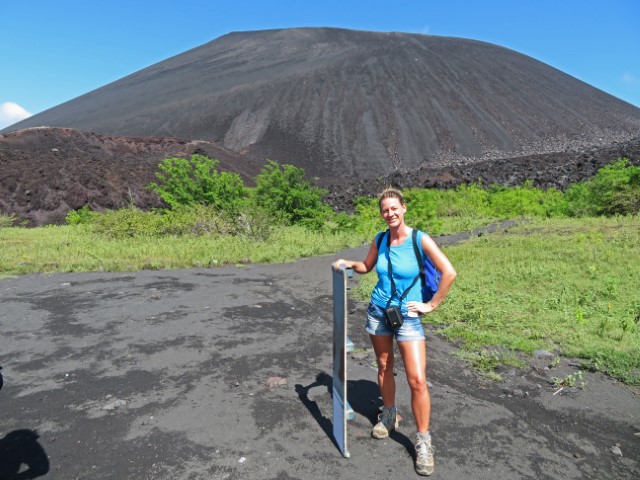 Junge Frau mit Brett zum Vulkan-Surfen in Nicaragua mit dem schwarzen Vulkan im Hintergrund