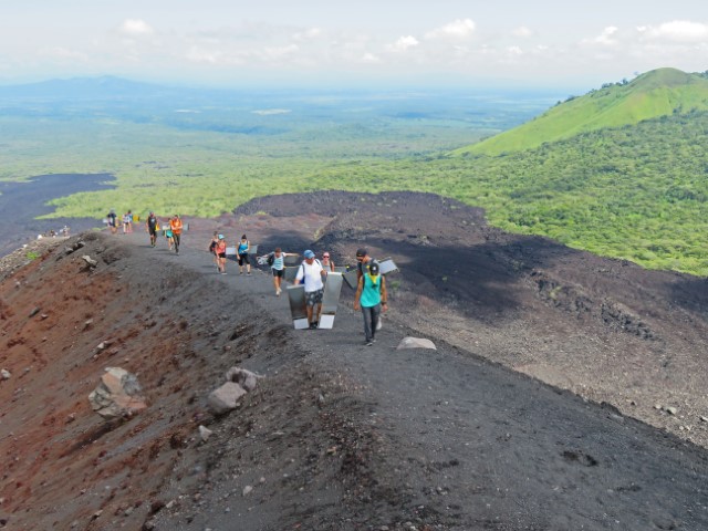 Leute mit Brettern zum Vulkan-Surfen steigen den schmalen schwarzen Weg zum Cerro Negro hoch