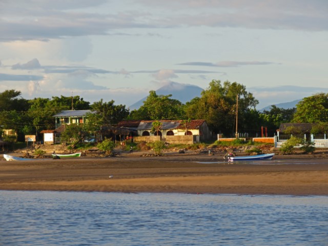 Blick vom Wasser auf einen Strand mit Hütten und einen Berg im Hintergrund