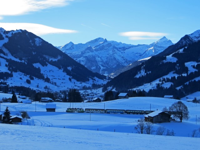 Blick auf Zug, der durch die verschneite Landschaft von Gstaad und vor der Bergkulisse fährt