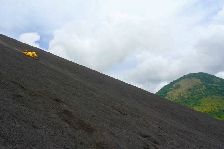 Mensch in gelbem Anzug surft liegend den Cerro Negro in Nicaragua runter