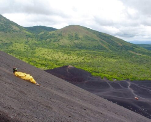 Mensch in gelbem Anzug surft liegend einen Vulkanin Nicaragua runter