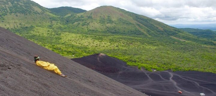 Mensch in gelbem Anzug surft liegend einen Vulkanin Nicaragua runter