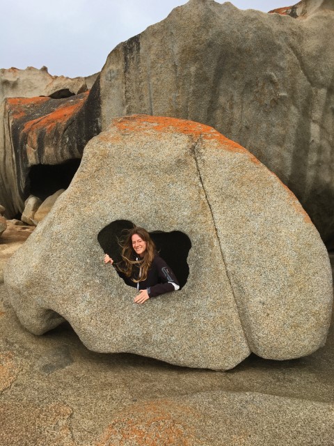 Junge Frau schaut durch ein Loch in einem großen Stein in Remarkable Rocks, Kangaroo Island