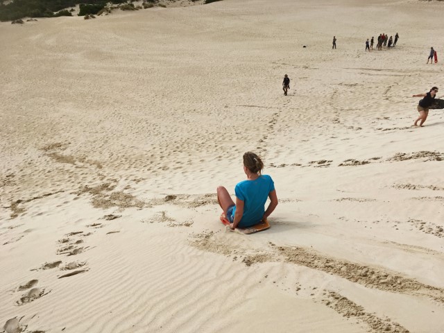 Frau fährtauf einem Sandboard eine Düne runter