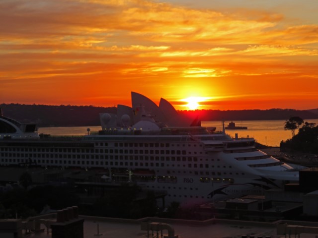 Sonnenuntergang hinter dem Opernhaus von Sydney mit einem Kreuzfahrtschiff im Vordergrund