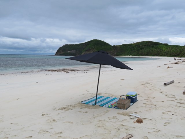 Picknickdecke, Korb und Sonnenschirm an einem weißen Sandstrand