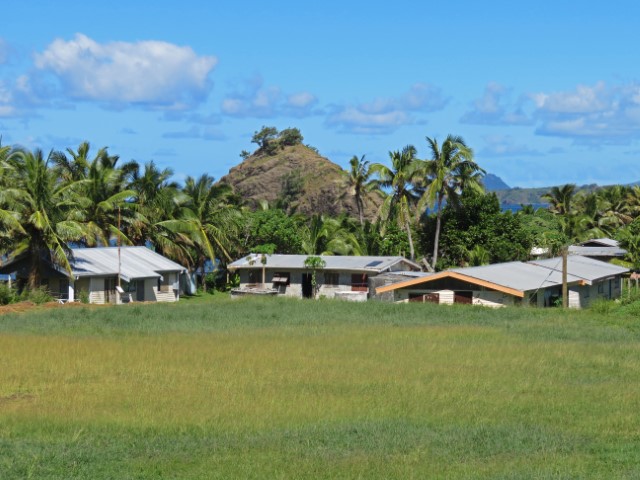 Normale flache Wohnhäuser auf Yasawa Island miz Palmen und Hügeln dahinter