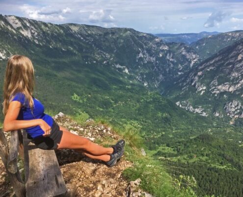 Junge Frau in Shorts sitzt auf einer Bank auf einem Gipfel und schaut über die Berge Montenegros