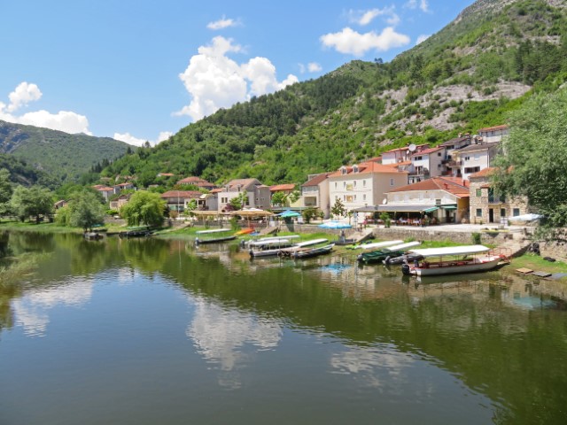 Rijeka Crnojevica, ein Dorf am Wasser mit kleinen Häusern und roten Dächern vor der grünen Hügellandschaft