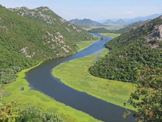 Blick über ein Flusstal mit grünen Bergen bis zum Horizont