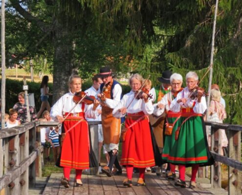 Schwedische Frauen in Tracht mit roten Röcken spielen im Gehen Geige