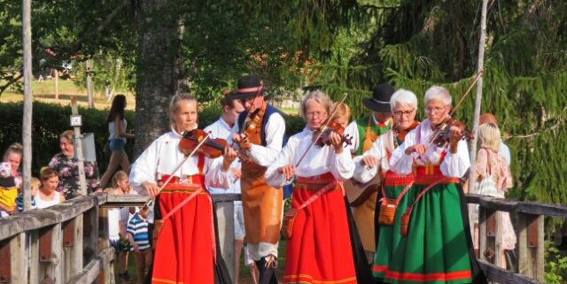 Schwedische Frauen in Tracht mit roten Röcken spielen im Gehen Geige