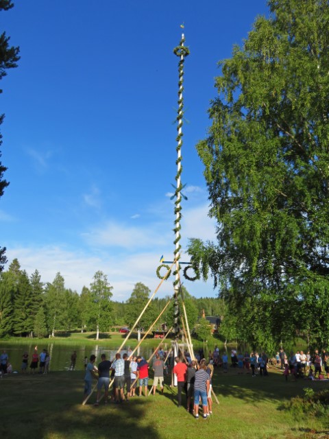 Mittsommerstange in Mångberg mit Kränzen, um die viele Menschen herumstehen