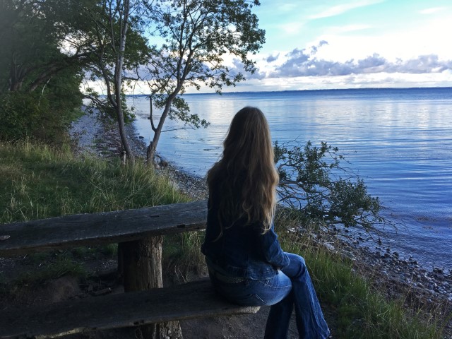 Frau mit langen Haaren sitzt auf einer Bank an der dänischen Ostsee