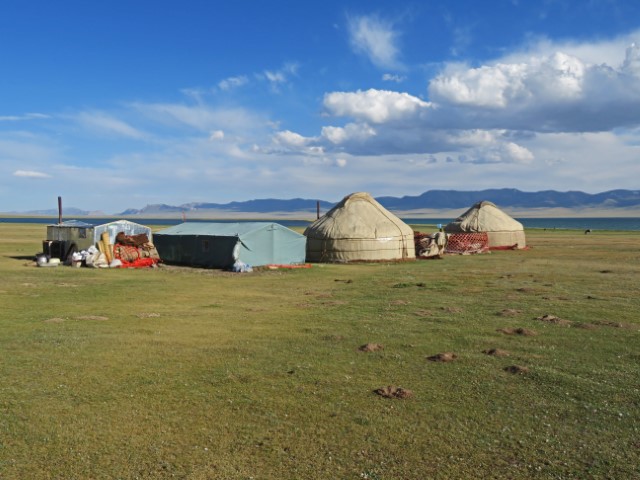 Jurten auf einer Wiese am Song Köl See mit Berglandschaft im Hintergrund