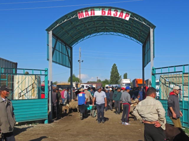 Torbogen mit Aufschrift Malbazar in Karakol, davor Männer mit Vieh