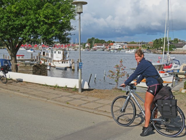 Junge Frau auf Fahrrad an einem Fjord mit Radwegschild für den Ostseeradweg