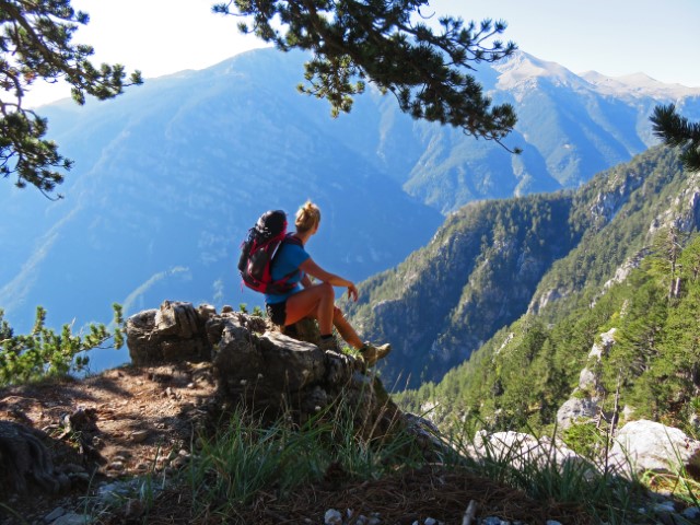 Junge Frau mit Rucksack sitzt auf Felsen und blickt auf Berge