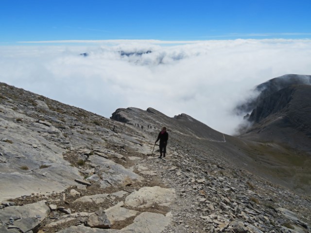 Frau wandert einen steilen Geröllhang in den Bergen hoch, hinter ihr Wolken